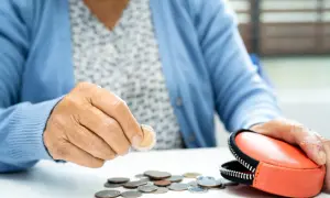 Ręka starszej osoby liczy monety obok portmonetki. Zastanawia się, jaka emerytura po 30 latach pracy przy najniższej krajowej ją czeka.