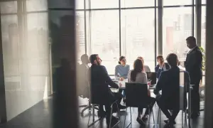 Grupa ludzi w garniturach podczas walnego zgromadzenia w sali konferencyjnej z widokiem na miasto.
