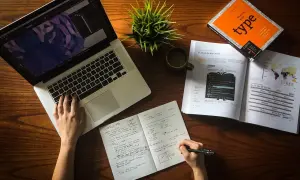Ręce pracują nad projektem, laptop, notatnik i książka o typografii. To idealne warunki do start up.