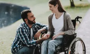 Mężczyzna wspiera kobietę na wózku inwalidzkim. Mimo że zabrano mi świadczenie pielęgnacyjne, ich uśmiechy i gesty mówią o sile miłości i wsparcia.