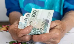 Dłonie trzymają polskie banknoty 100 zł. Zastanawiasz się, ile komornik może zabrać z emerytury?