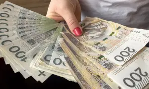 Dłoń trzyma wachlarz polskich banknotów 100 i 200 zł. To może być nagroda jubileuszowa nauczycieli.