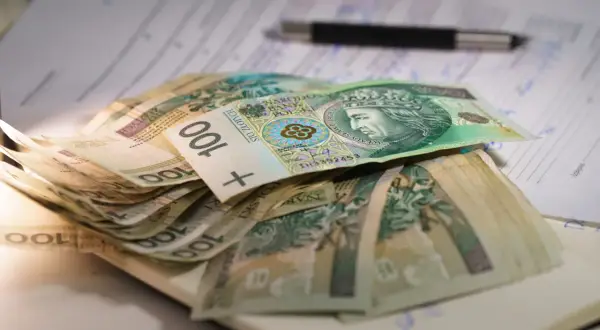 Stos stu-złotowych banknotów leży na dokumentach. W tle widać długopis. To może być pomoc dla osób z mops znaczny stopień niepełnosprawności.