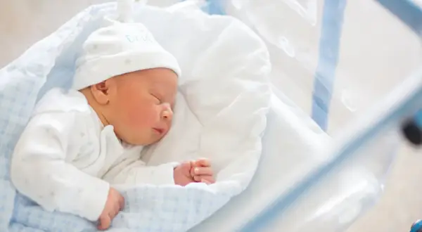 Śpiący noworodek w czepku z napisem "DADDY". To maleństwo zasługuje na becikowe, które pomoże rodzicom w pierwszych miesiącach życia.