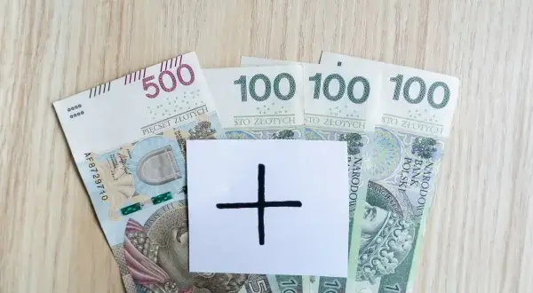 Polskie banknoty 500 i 100 zł. Na białej kartce symbol plusa. Czy to zapowiedź wyższej pensji?