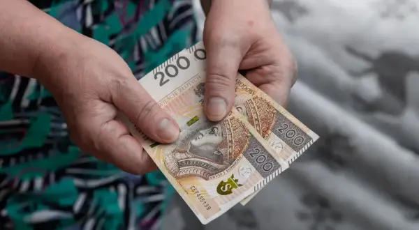 Dwie stuzłotówki w dłoniach, symbol wsparcia z MOPS. Zasiłek pielęgnacyjny na codzienne potrzeby.