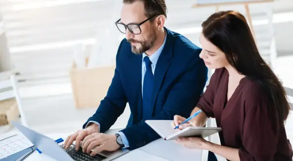 Biznesmeni pracują nad inwentaryzacją, mężczyzna pisze na laptopie, kobieta notuje.