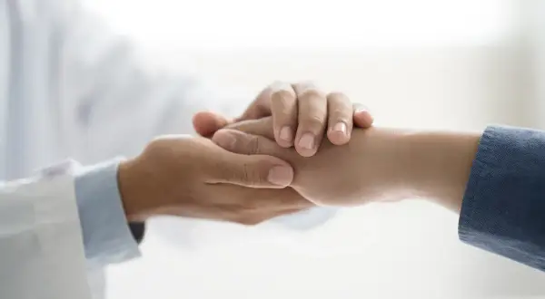 Lekarz w białym fartuchu trzyma za rękę pacjenta.
