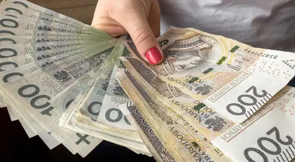Dłoń trzyma wachlarz polskich banknotów 100 i 200 zł. To może być nagroda jubileuszowa nauczycieli.