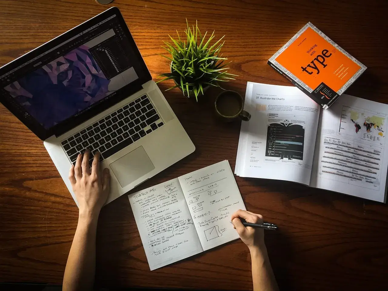 Ręce pracują nad projektem, laptop, notatnik i książka o typografii. To idealne warunki do start up.