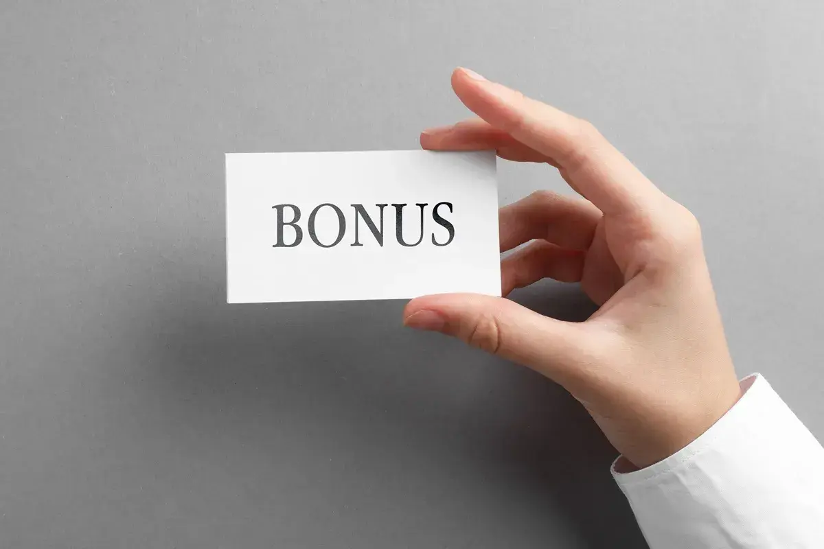 Dłoń trzyma kartkę z napisem "BONUS". To może być zapowiedź dodatku stażowego, który czeka na pracownika.