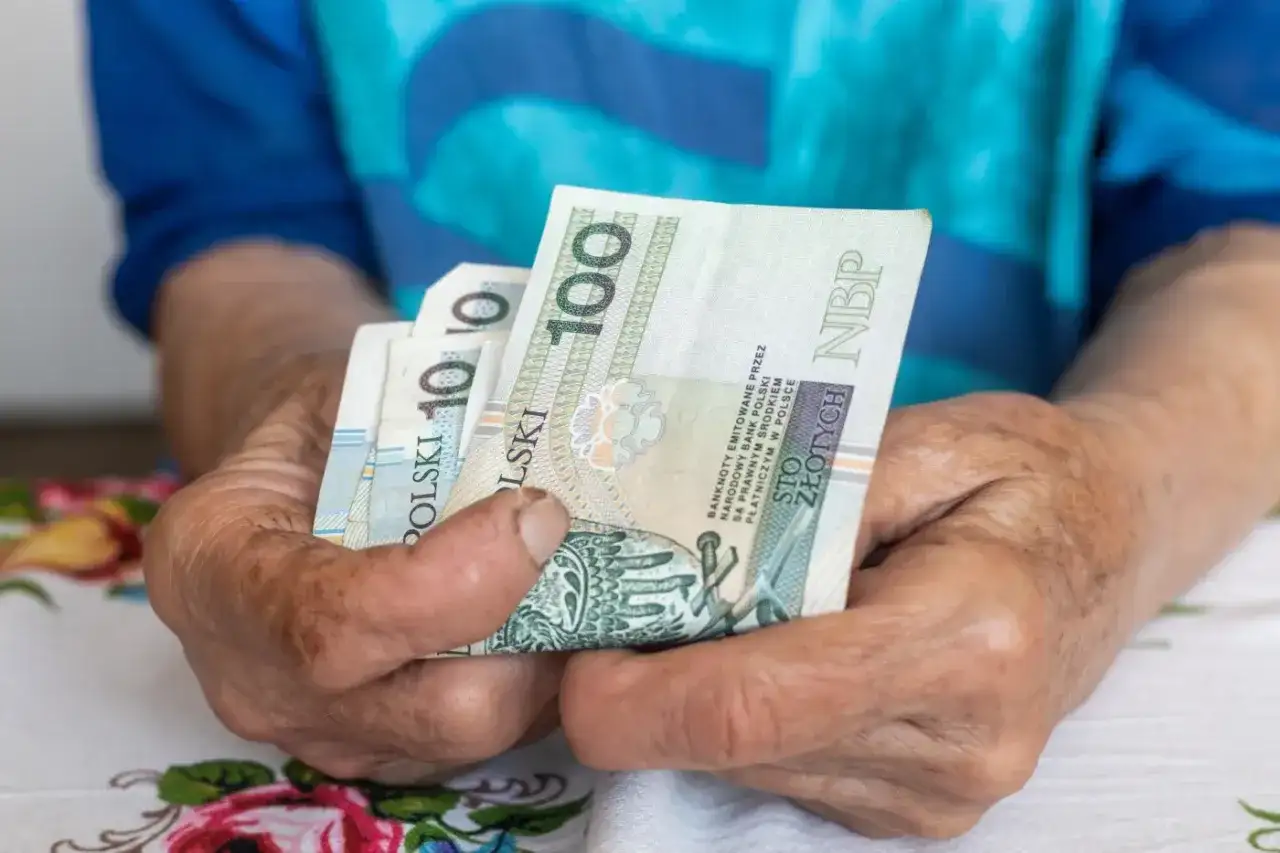 Dłonie trzymają polskie banknoty 100 zł. Zastanawiasz się, ile komornik może zabrać z emerytury?