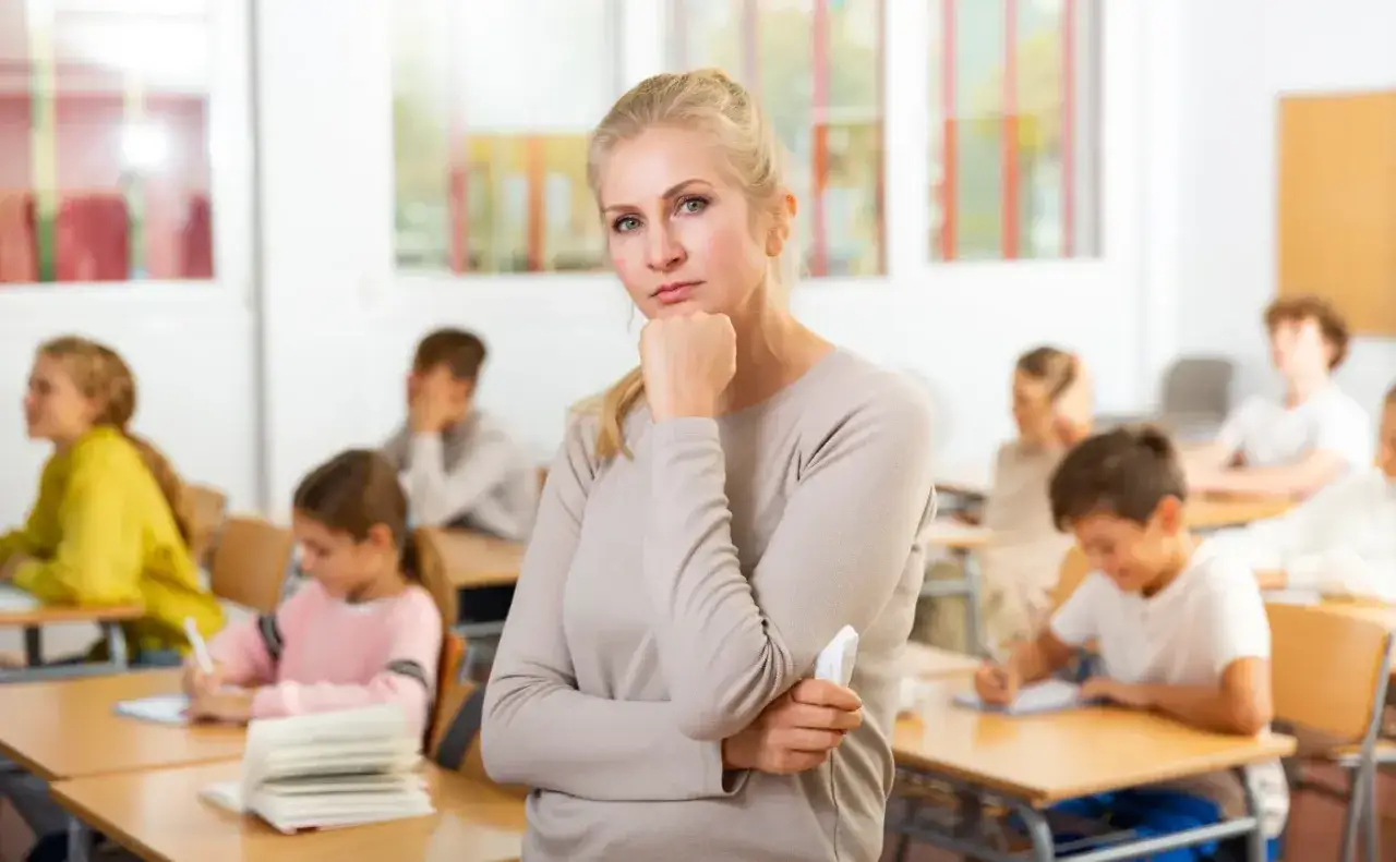 Nauczycielka zamyślona w klasie, uczniowie pracują. Czy doczekamy się podwyżki dla nauczycieli w 2026 roku?