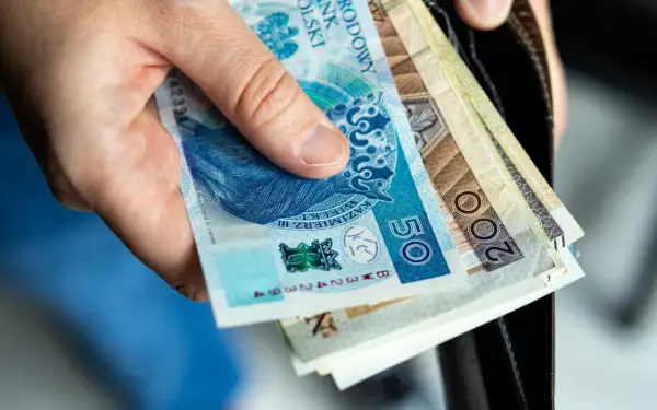 Dłoń trzyma polskie banknoty 50 i 200 zł. Zastanawiasz się nad nowymi zasadami przejścia na emeryturę? Tabela z wyliczeniami pomoże Ci to zrozumieć.
