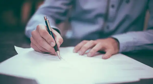 Dłoń pisze długopisem na dokumencie. Może to być umowa, faktura, a nawet wypełnianie formularza NIP-8.