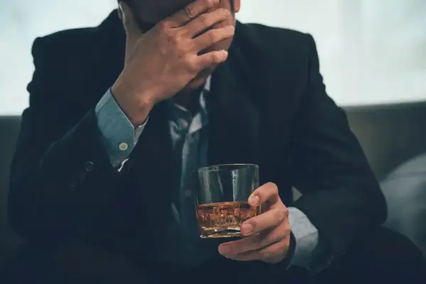 Mężczyzna w garniturze trzyma szklankę z whisky, opierając czoło na dłoni. Może to symbolizować problemy, stres, a nawet **renta alkoholowa**.